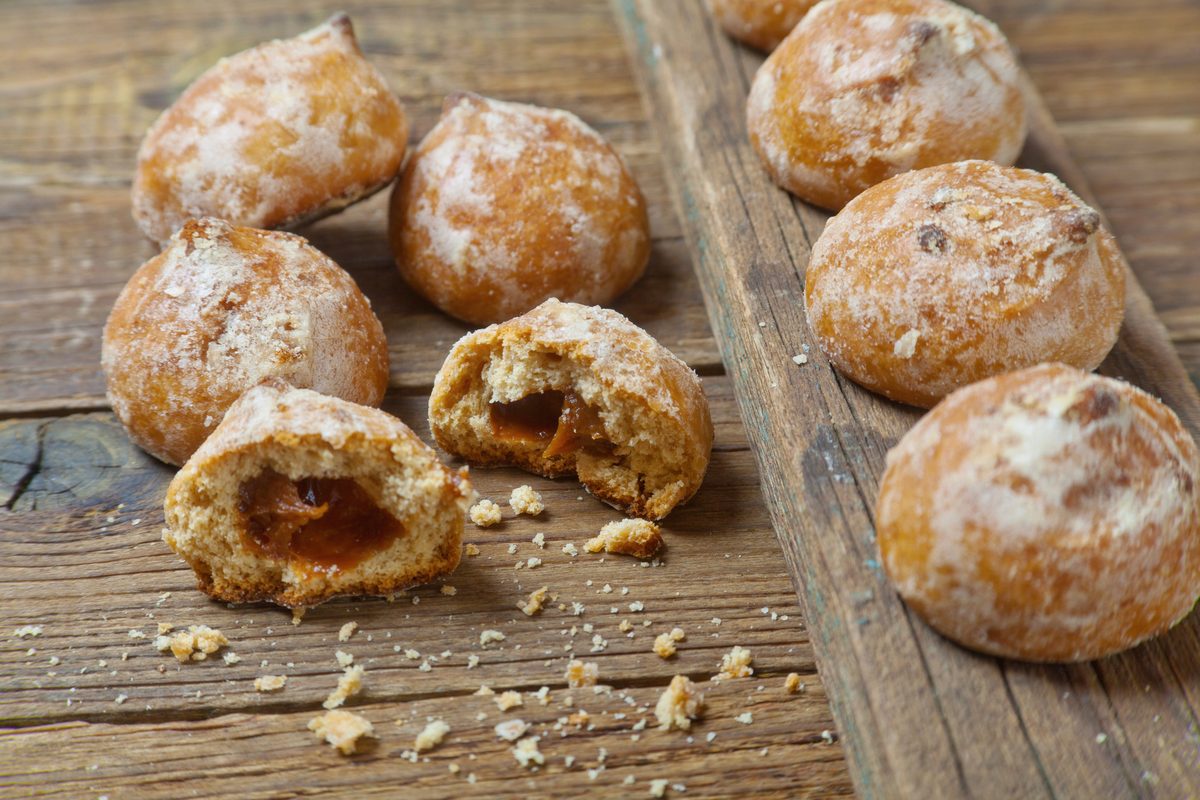 Small round spiced cookies on a wooden table, one broken to show the filling