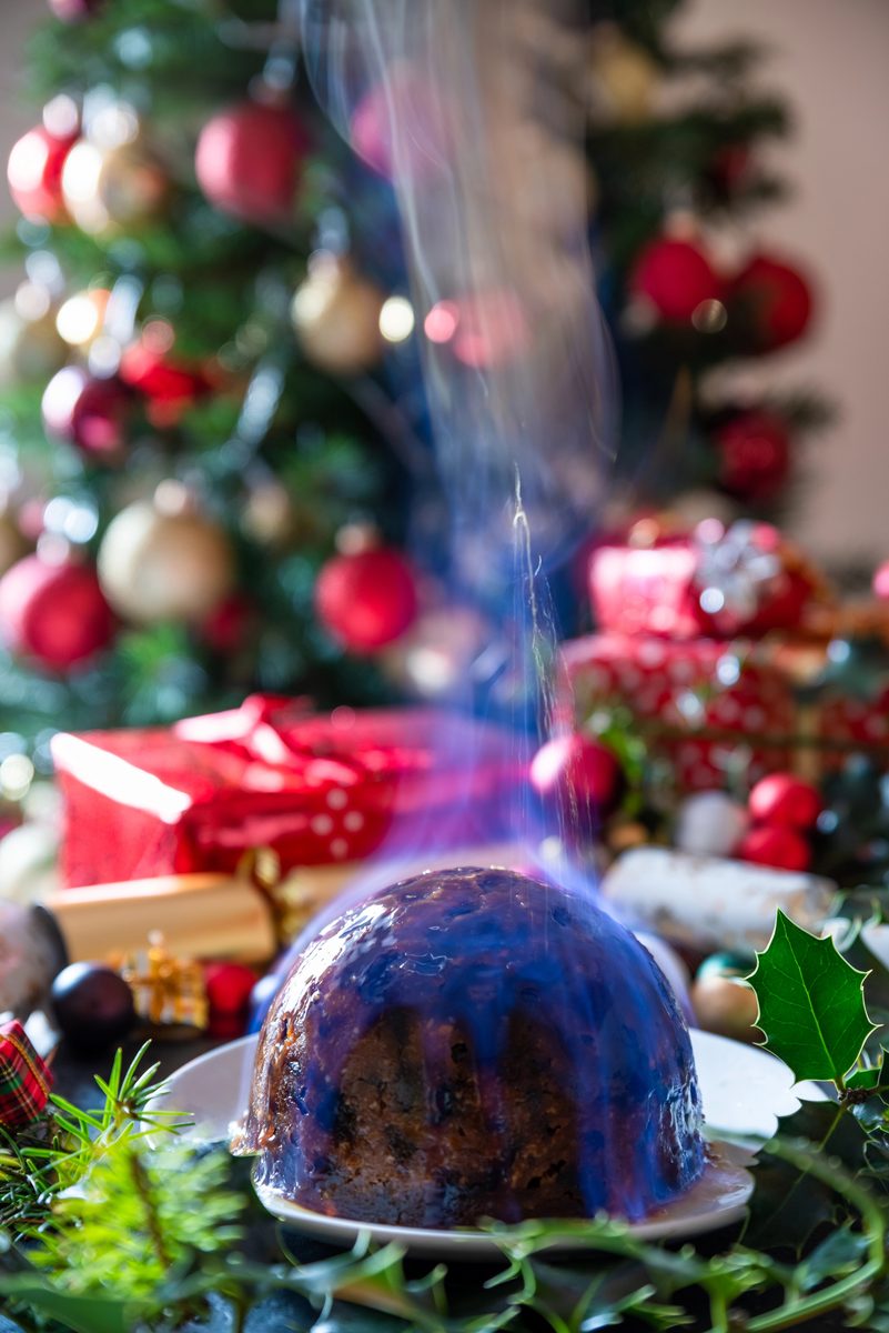 Flaming Christmas pudding beside a decorated Christmas tree