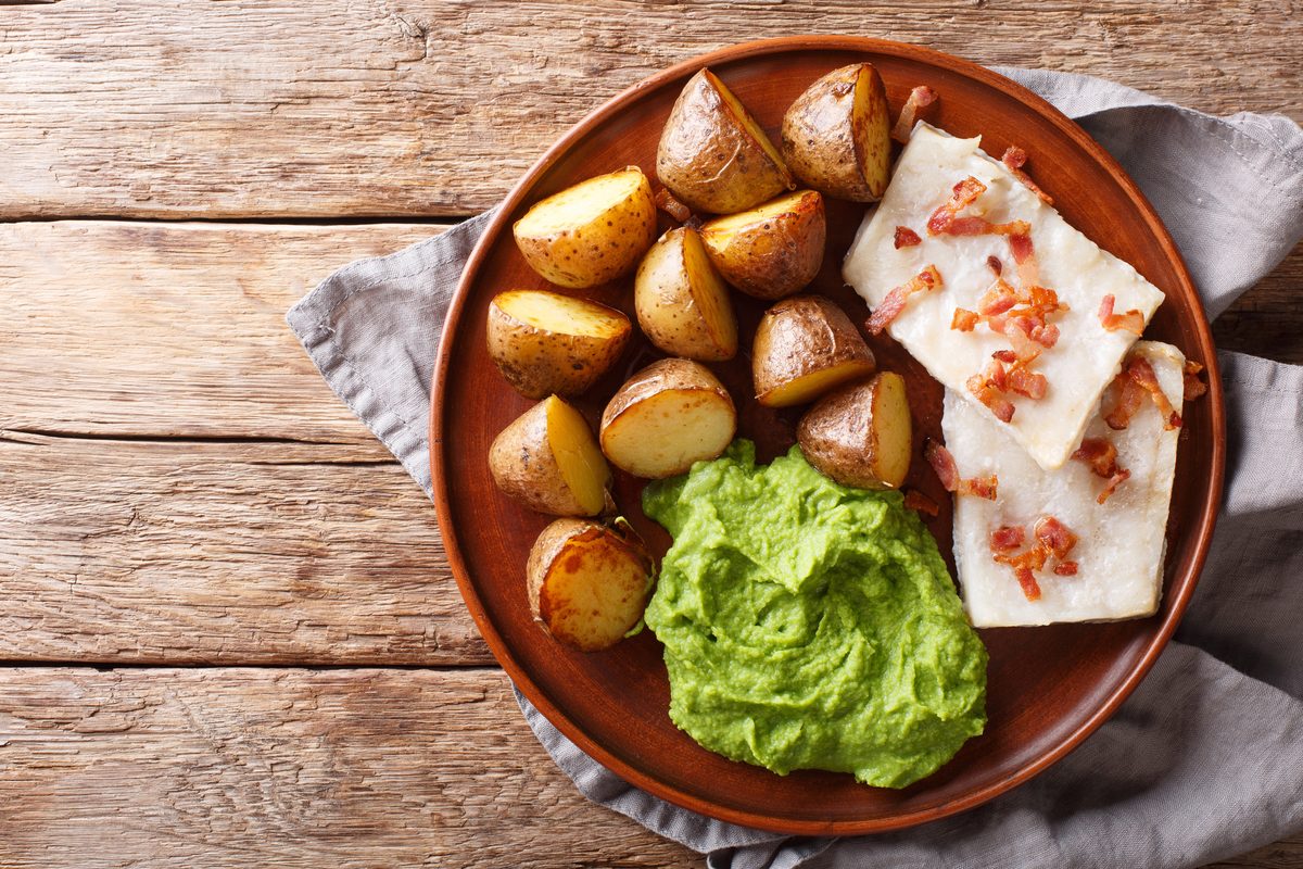 Lutefisk with green pea purée, boiled potatoes and bacon on a plate