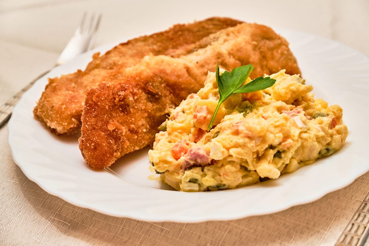 Fried carp fillets served with potato salad on a white plate