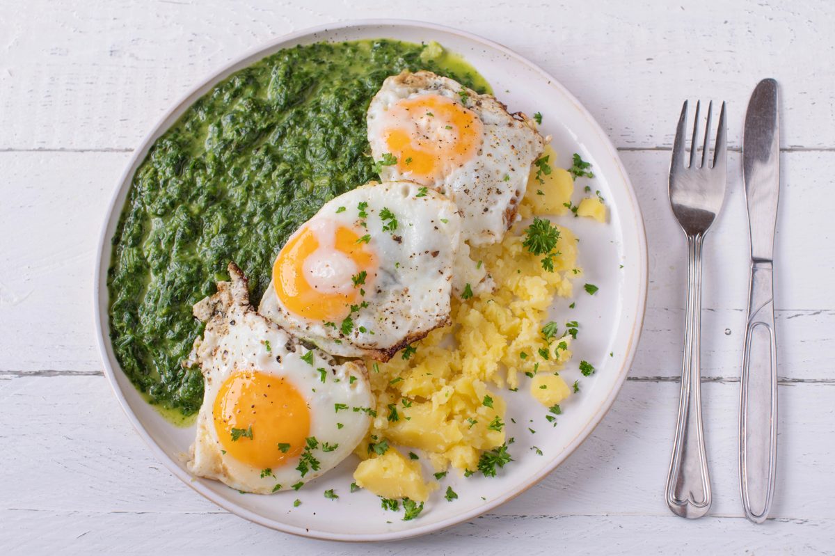 Creamed spinach with two fried eggs and potatoes on a white plate