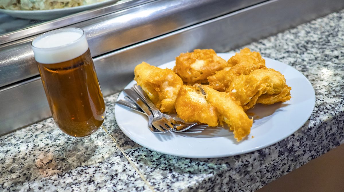 Battered salt cod strips on a plate with a glass of beer