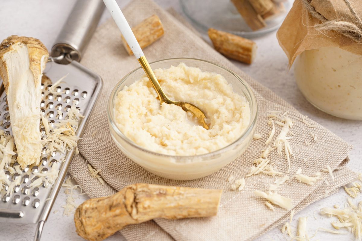 Horseradish cream in a bowl with fresh horseradish roots and a grater