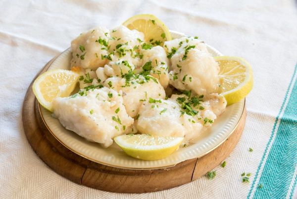 White cod pieces with olive oil, parsley and lemon on a plate