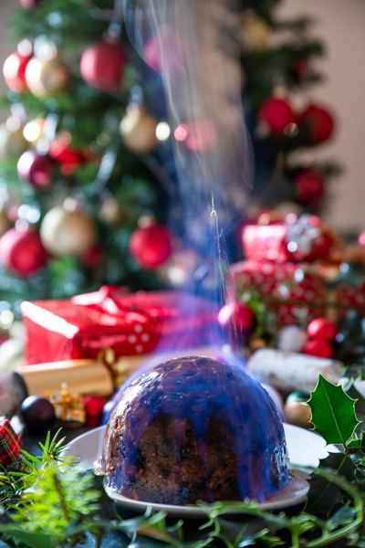 Flaming Christmas pudding beside a decorated Christmas tree