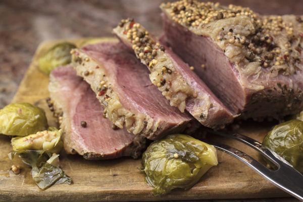 Sliced spiced beef on a wooden board with peppercorns and Brussels sprouts