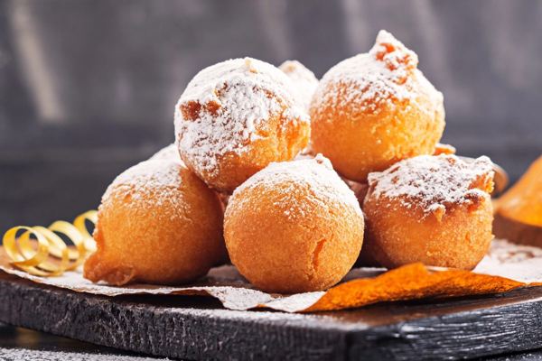 Fried Christmas dough balls dusted with sugar on a dark board