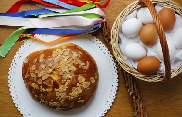 Round mazanec Easter bread topped with flaked almonds, next to a basket of eggs