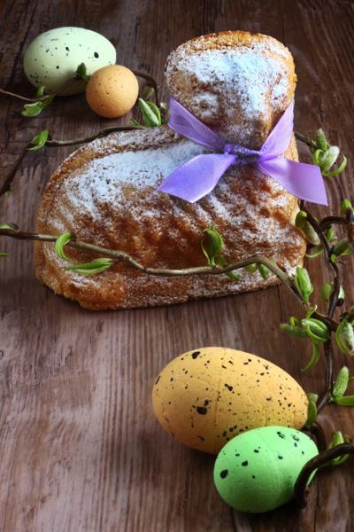 Lamb-shaped Easter cake dusted with sugar, with a purple ribbon and Easter eggs