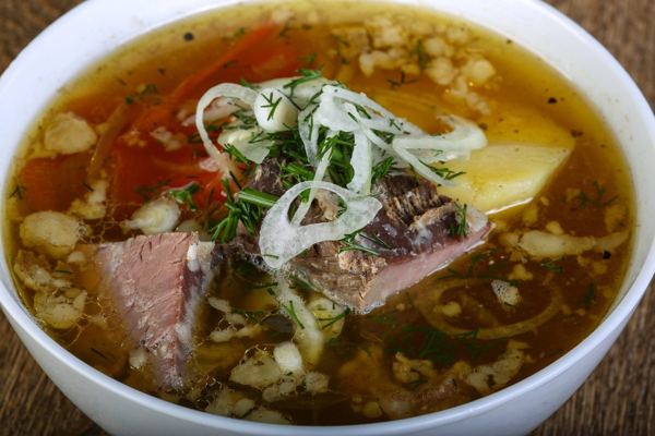 Lamb soup with vegetables and sliced onion in a white bowl